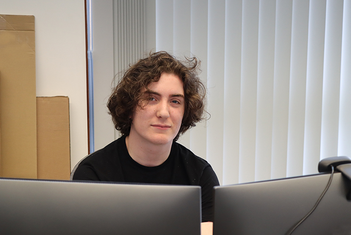 Dylan yn y swyddfa tu nol i sgriniau cyfrifiadur